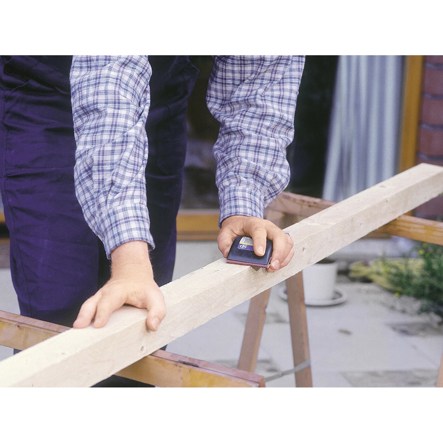 Rzemieślnik szlifuje drewno za pomocą ręcznego klocka ściernego LUX 70x130 mm. Prace szlifierskie z materiałami ściernymi.