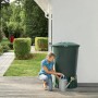 Ciemnozielony zbiornik na deszczówkę z kobietą i konewką w ogrodzie.