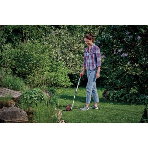 Kobieta używa akumulatorowych nożyc do trawy w ogrodzie. Precyzyjna pielęgnacja trawnika za pomocą nożyc do trawy.