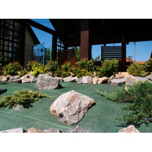 Zielona włóknina/folia ogrodowa z kamieniami i roślinami.