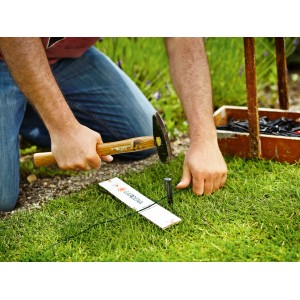 Instalacja przewodu ograniczającego robota koszącego Gardena za pomocą młotka i kołka w ogrodzie.