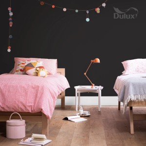 Pokój dziecięcy z ciemno pomalowaną ścianą i dwoma łóżkami. Kolorowa farba do ścian tworzy atmosferę.