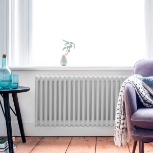 Biały grzejnik (t.b.t.) przed oknem w salonie.