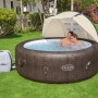 Osłona przeciwsłoneczna Bestway LAY-Z-SPA nad brązowym jacuzzi z parą w ogrodzie.