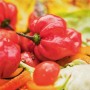 Czerwone, okrągłe papryczki chili na liściach sałaty i warzywach.