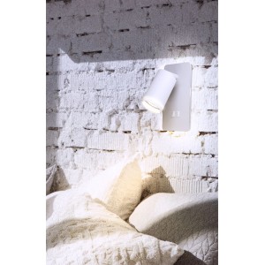 Biały kinkiet t.b.t. na białej ceglanej ścianie nad łóżkiem.