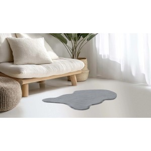 Szary, nieregularny dywan z długim włosiem przed sofą i oknem.