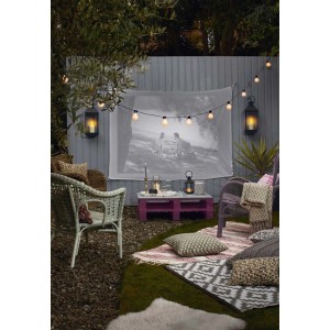 Scena ogrodowa z kinem na świeżym powietrzu, girlandą świetlną, lampionami i przytulnymi miejscami do siedzenia.