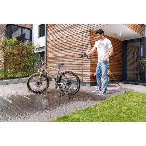 Mężczyzna czyści rower urządzeniem do czyszczenia powierzchni płaskich t.b.t. przed domem.