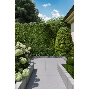 Szare płyty tarasowe i chodnikowe t.b.t. w ogrodzie z zielonym żywopłotem.