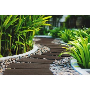 Ścieżka ogrodowa z brązowymi podestami t.b.t. i żwirem między zielonymi roślinami.