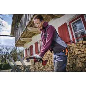 Kobieta piłuje drewno czerwoną pilarką akumulatorową. Elektryczna pilarka łańcuchowa do ogrodu.