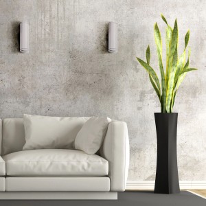 Dwa szare kinkiety na betonowej ścianie nad białą sofą i rośliną.