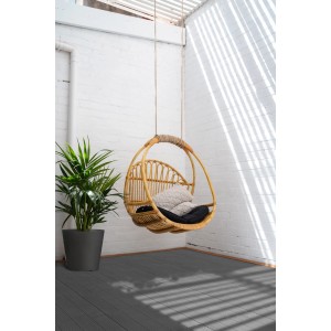 Rattanowy fotel wiszący z poduszkami na szarej podłodze tarasowej.