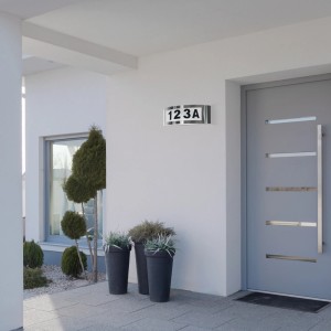 Nowoczesna lampa z numerem domu t.b.t. jako kinkiet zewnętrzny na białej ścianie domu.