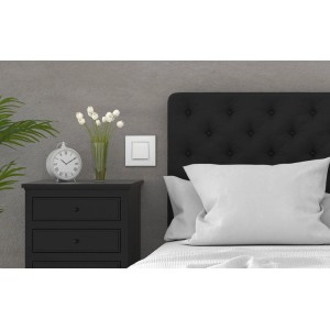 Biały włącznik t.b.t. obok łóżka na szarej ścianie.