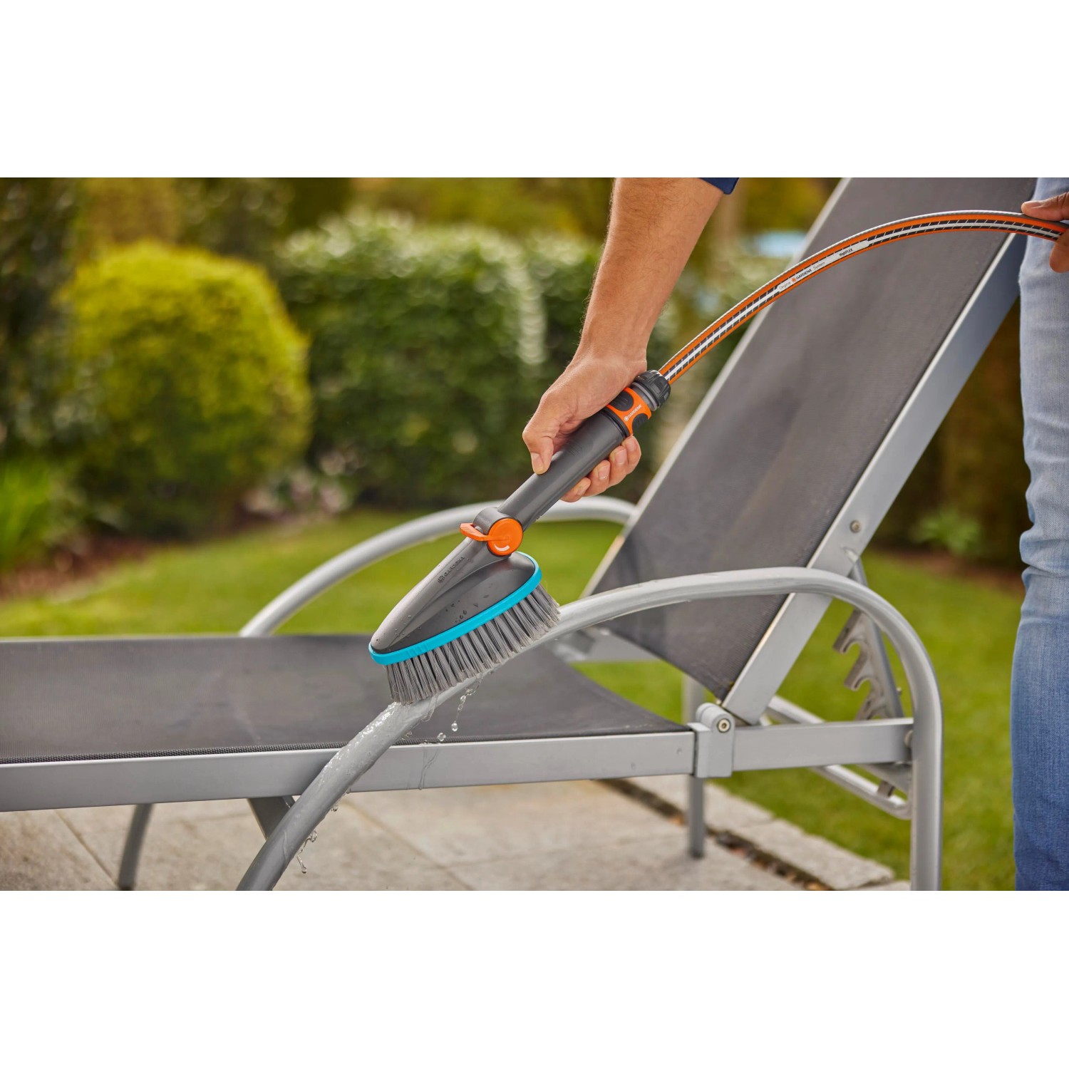 Gardena Cleansystem Szczotka ręczna Soft M z przyłączem węża w użyciu do czyszczenia leżaka ogrodowego.