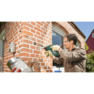 Mężczyzna wierci w ceglanej ścianie młotowiertarką Bosch PBH 2100 RE ZB.