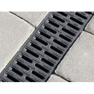 Czarny, plastikowy kanał odwadniający ACO Hexaline 2.0 z rusztem Microgrip między kostką brukową.