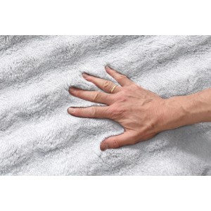 Dłoń na puszystym, jasnoszarym dywanie z długim włosiem. Miękka tekstura.