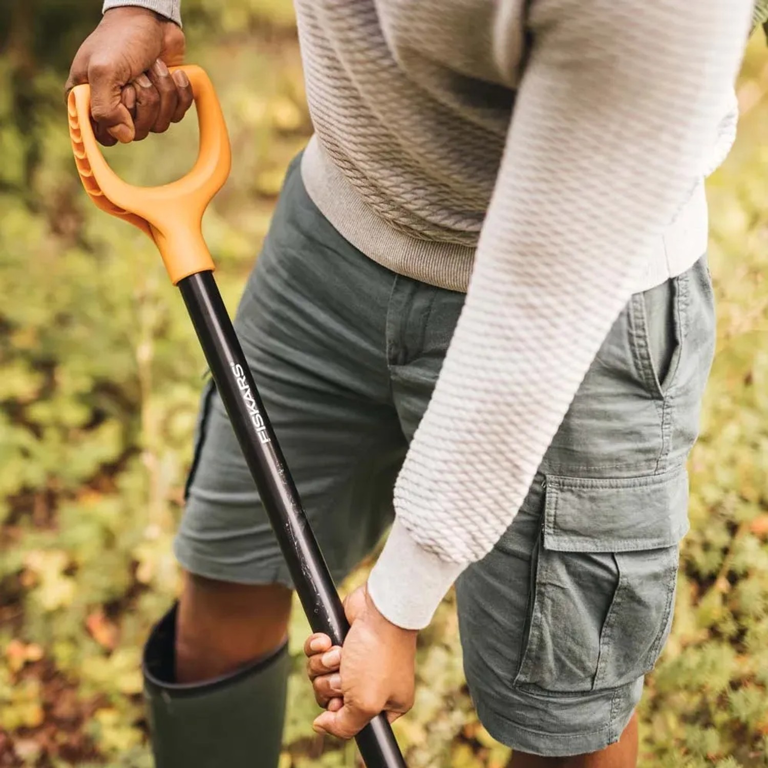 Mężczyzna używa szpadla Fiskars w ogrodzie. Narzędzie ogrodowe z pomarańczową rączką.