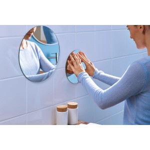 Kobieta mocuje okrągłe, samoprzylepne lustro t.b.t. do ściany w łazience.