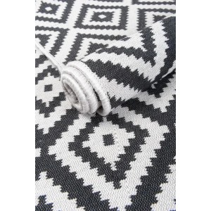 Dywan z krótkim włosiem t.b.t. z graficznym wzorem w kolorze czarno-białym, częściowo zwinięty.