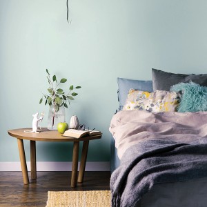 Przestrzeń mieszkalna z miętowo zieloną farbą na ścianie. Dekoracja ze stołem, łóżkiem i akcesoriami.