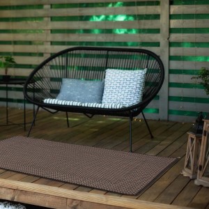 Brązowy dywan z krótkim włosiem t.b.t. na drewnianym tarasie z miejscami do siedzenia w tle.