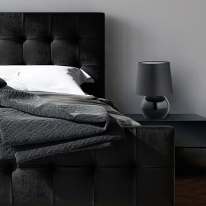 Czarna lampa stołowa t.b.t. na szafce nocnej obok łóżka. Lampa dekoracyjna.