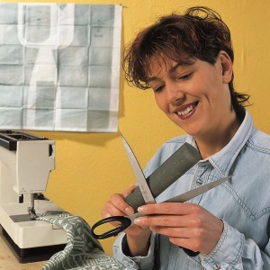 Kobieta ostrzy nożyczki osełką Schärffix przed maszyną do szycia.