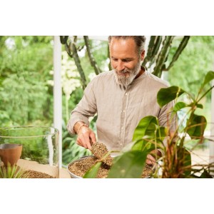 Mężczyzna łopatą wsypuje ziemię do doniczki. Ziemia uniwersalna do roślin doniczkowych.