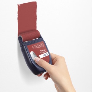 Ręka maluje czerwoną farbę na ścianie wałkiem. Tester farb do ścian.