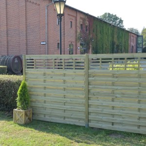 Jasne drewniane panele ogrodzeniowe z kategorii ogrodzeń ogrodowych przed budynkiem z cegły.