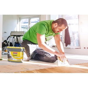 Mężczyzna układa parkiet za pomocą kleju Soudal Parkettkleber 68A z żółtego 15 kg wiadra.