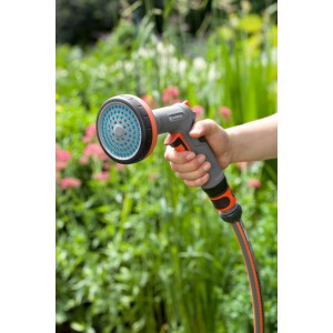 Gardena Comfort Zraszacz do grządek w użyciu: Ręka trzyma szary zraszacz ogrodowy z niebieską główką zraszającą przed zieloną grządką.