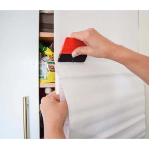 Zestaw do aplikacji folii d-c-fix w użyciu: Folia wygładzana na szafce raklem.