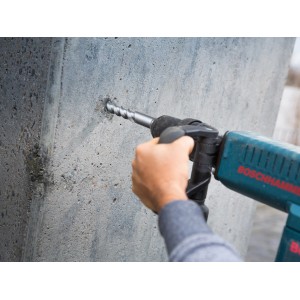 Wiertło LUX Hammer Classic SDS-Max wierci otwór w betonowej ścianie za pomocą wiertarki udarowej.
