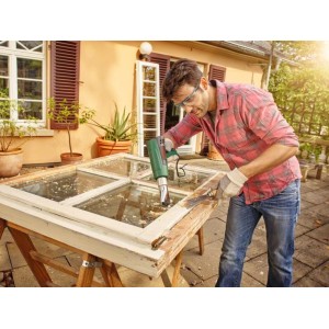 Mężczyzna usuwa farbę z ramy okiennej za pomocą opalarki.