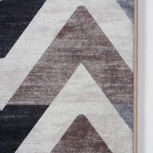 Zbliżenie dywanu z krótkim włosiem z abstrakcyjnym wzorem zygzaków w odcieniach szarości i brązu.