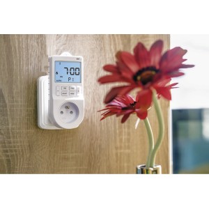 Biały zegar sterujący t.b.t. do grzejników z wyświetlaczem i gniazdkiem na drewnianej ścianie.