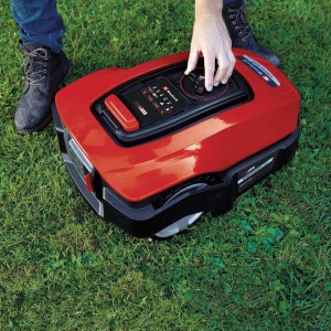 Czerwony robot koszący Einhell Freelexo 1200 LCD BT na trawie, obsługa wyświetlacza.