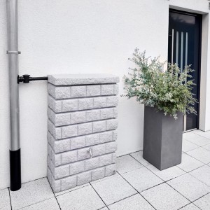 Garantia Rocky Junior 300 l Light Granite zbiornik ścienny imitujący kamień obok rury spustowej i donicy.