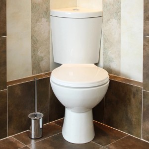 Białe kompaktowe WC ze spłuczką i szczotką toaletową w łazience.