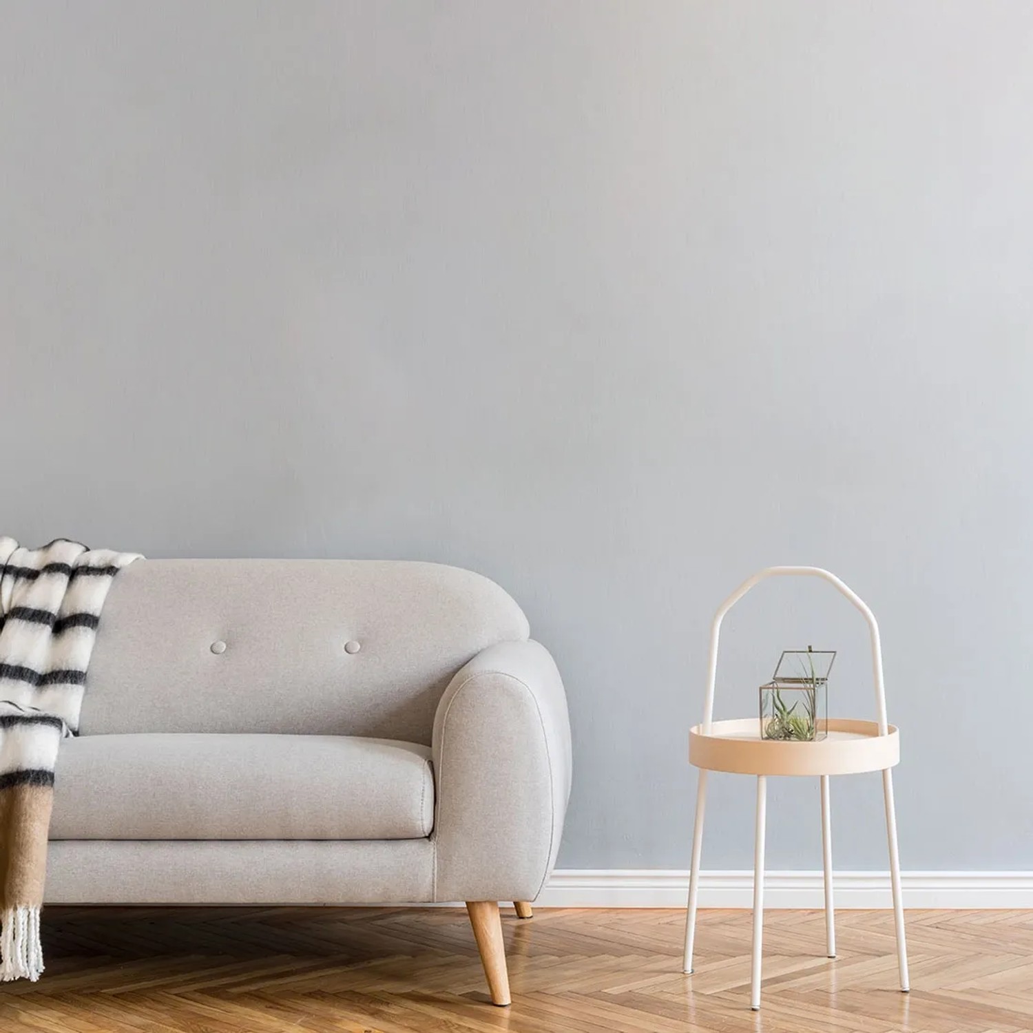Salon z szarą ścianą, sofa z kocem i stolik z dekoracją.