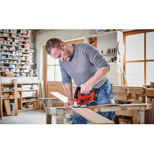 Mężczyzna piłuje drewno czerwoną wyrzynarką. Wyrzynarki do precyzyjnych cięć.