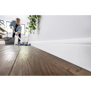 Biała listwa przypodłogowa (t.b.t.) na ścianie, czyszczenie podłogi w tle.