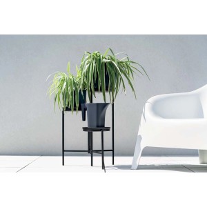 Szara konewka t.b.t. na czarnym stojaku na rośliny, obok białe krzesło.