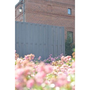 Szary drewniany płot (t.b.t.) przed budynkiem z cegły z różowymi kwiatami na pierwszym planie.