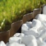Brązowe plastikowe obrzeże trawnikowe t.b.t. obramowane białymi kamykami dekoracyjnymi.